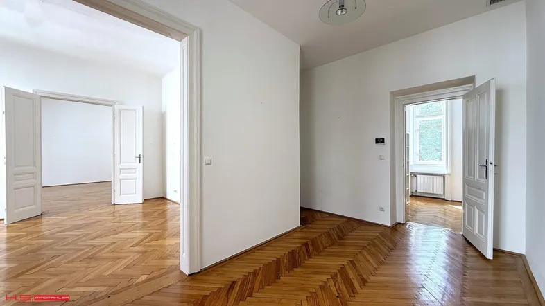 Geräumiges Zimmer mit Fischgrätparkett und hohen Türen, das in weitere Räume führt.