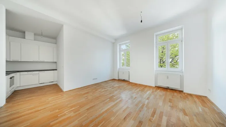 Helles Wohnzimmer mit Parkettboden und integrierter Küchenzeile, ideal für offenes Wohnen.