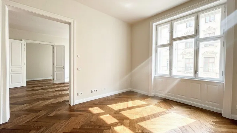 Helles Zimmer mit Fischgrätparkett und großen Fenstern, das viel Tageslicht hereinlässt.