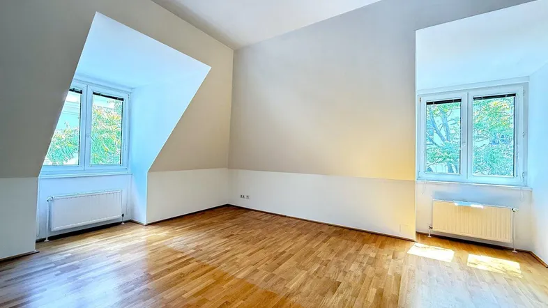 Helles Zimmer im Dachgeschoss mit Holzboden und schrägen Wänden, ideal als Schlaf- oder Wohnbereich.