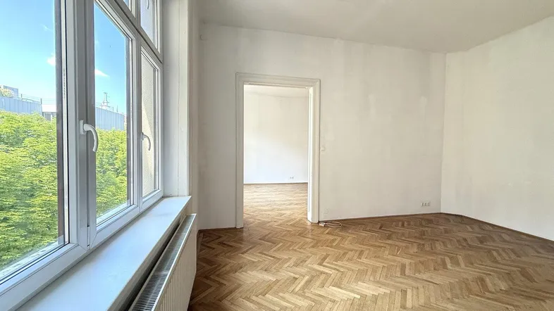 Helles Zimmer mit Fischgrätparkett und großen Fenstern, die einen Blick ins Grüne bieten.