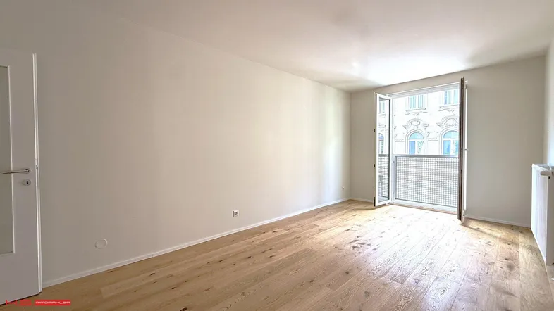 Helles Zimmer mit Holzboden und französischem Balkon, bereit zur individuellen Gestaltung.