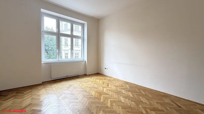 Helles Zimmer mit Fischgrätparkett und großem Fenster, das viel Tageslicht hereinlässt.