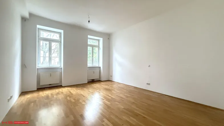 Heller, leerer Raum mit Parkettboden und zwei Fenstern, ideal als Wohnzimmer oder Schlafzimmer.