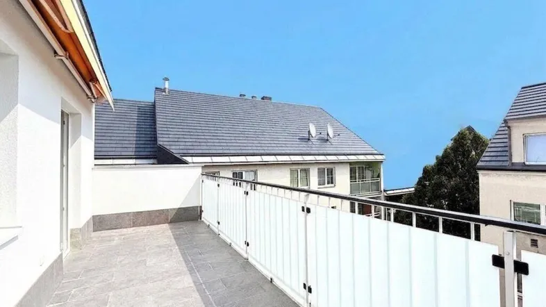 Geräumige Terrasse mit modernen Fliesen und Blick auf die umliegenden Gebäude und den blauen Himmel.