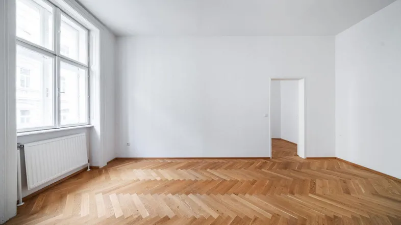 Geräumiges, helles Zimmer mit klassischem Fischgrätparkett und großen Fenstern.