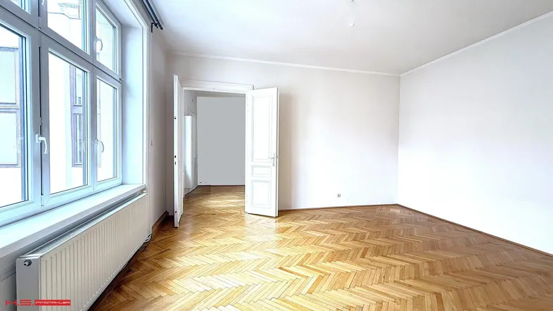 Helles Zimmer mit Fischgrätparkett und großen Fenstern, das viel Tageslicht hereinlässt.