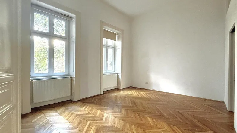 Helles Zimmer mit klassischem Fischgrätparkettboden und großen Fenstern, die viel Tageslicht hereinlassen.