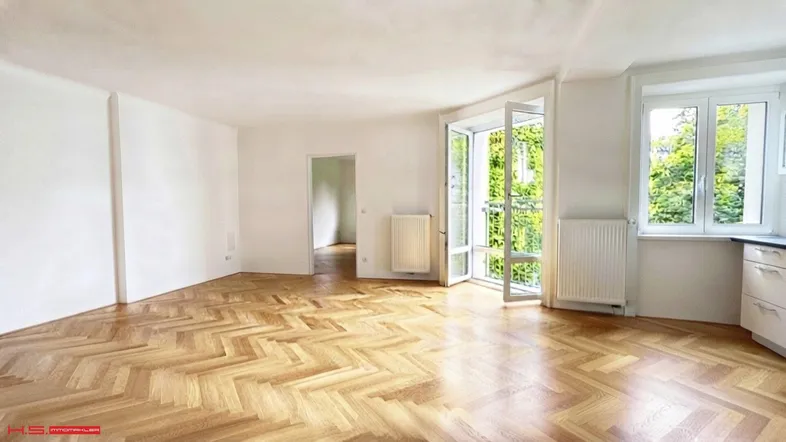 Helles Wohnzimmer mit Fischgrätparkett, weißen Wänden und Zugang zu einem französischen Balkon.