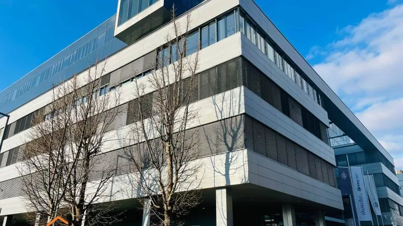Modernes Bürogebäude mit Glasfassade und horizontalen Lamellen unter blauem Himmel.
