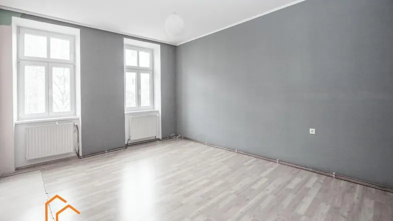 Helles Zimmer mit grauen Wänden und hellem Laminatboden, bereit zur individuellen Gestaltung.