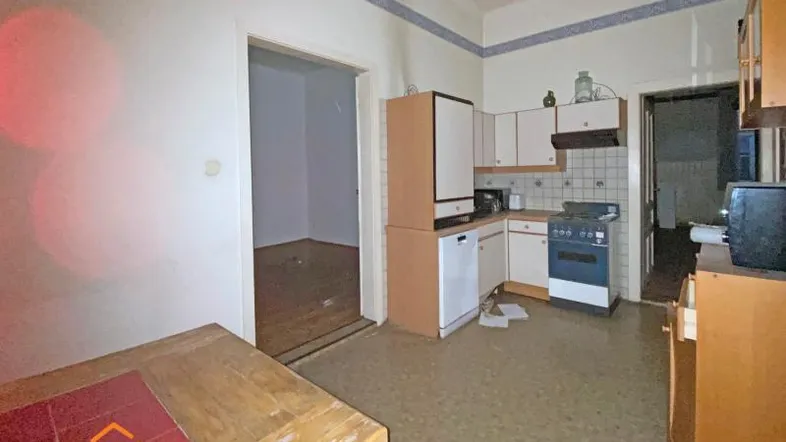 Alte Küche mit einfacher Ausstattung, Essbereich und Blick in einen leeren Raum.