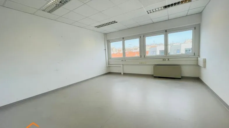 Leeres Büro mit großen Fenstern, abgehängter Decke und hellem Bodenbelag, bereit zur individuellen Gestaltung.