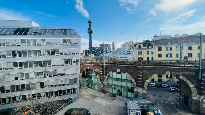 Blick aus dem Fenster auf eine städtische Umgebung mit modernen Gebäuden, einer historischen Brücke und einem Parkplatz.