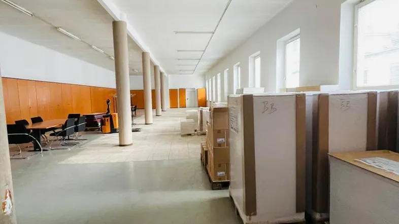 Geräumiger Büroraum mit hohen Decken, Säulen, großen Fenstern und Betonboden, teilweise mit Kartons belegt.