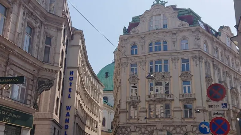Historische Gebäude säumen eine belebte Straße in der Stadt, mit Autos und Fußgängern unter blauem Himmel.