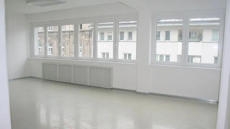 Heller Büroraum mit großen Fenstern, die viel Tageslicht hereinlassen und einen Blick auf die umliegenden Gebäude bieten.