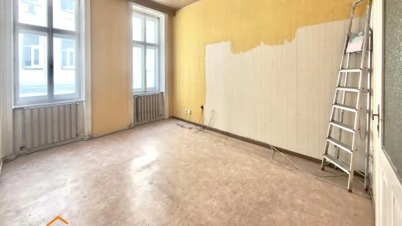 Renovierungsbedürftiger Raum mit gelben Wänden, zwei Fenstern und einer Leiter, bereit zur Neugestaltung.