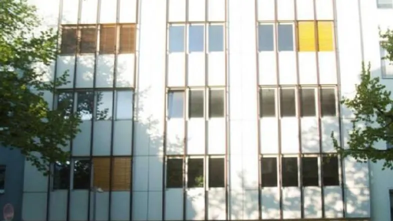 Modernes Bürogebäude mit vielen Fenstern und Jalousien in einer städtischen Umgebung.