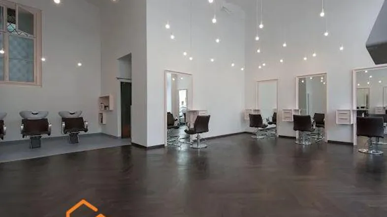 Geräumiger, heller Salonbereich mit hohen Decken, dunklem Fischgrätparkett und mehreren Frisierplätzen.