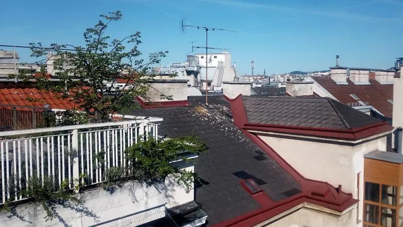 Blick über die Dächer der Stadt mit einem kleinen Balkon oder einer Terrasse und blauem Himmel.