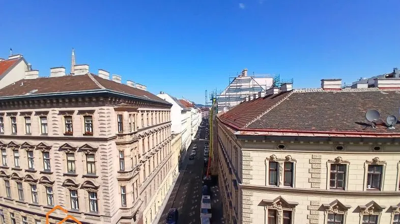 Blick über eine belebte Stadtstraße mit historischen Gebäuden und blauem Himmel an einem sonnigen Tag.
