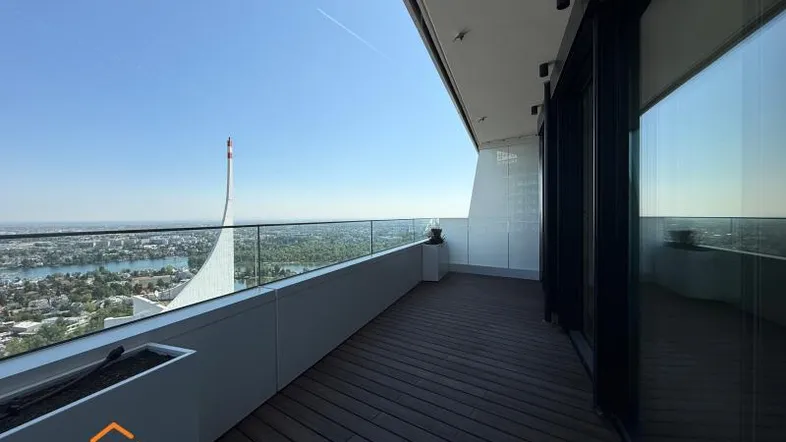 Geräumiger Balkon mit Holzboden, Glasgeländer und weitem Blick über die Stadt und den See.