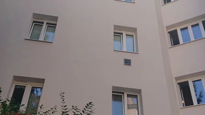 Fassade eines Mehrfamilienhauses mit mehreren Fenstern und umgebenden Bäumen.
