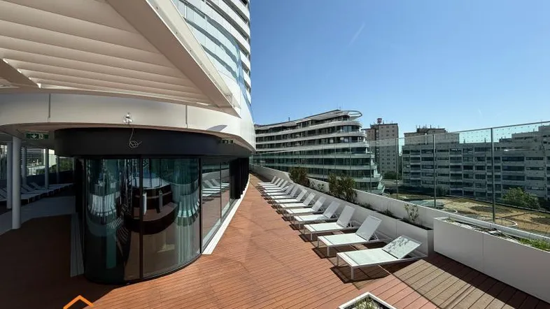 Große Sonnenterrasse mit vielen Liegestühlen und Blick auf moderne Gebäude in der Stadt.