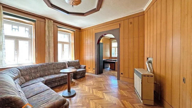 Geräumiges Wohnzimmer mit Fischgrätparkett, Holzvertäfelung und dekorativer Decke, bietet viel Platz.