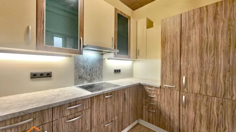 Moderne Küche mit Holzfronten, heller Arbeitsplatte, Induktionskochfeld und integrierter Beleuchtung.