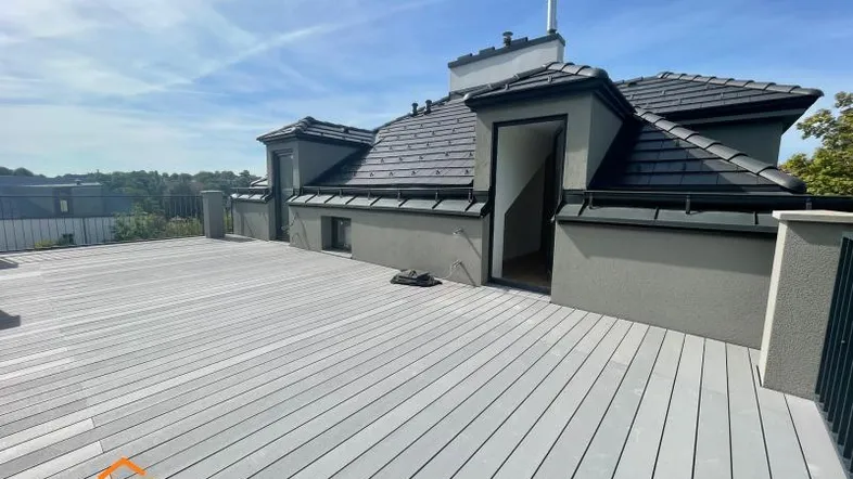 Große Dachterrasse mit modernem Holzboden und Blick auf die Umgebung unter blauem Himmel.