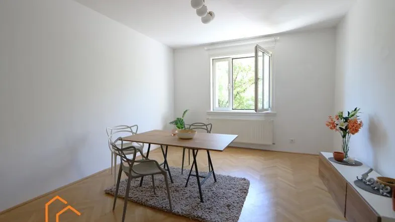 Helles Zimmer mit Fischgrätparkett, Esstisch und Blick ins Grüne durch das Fenster.
