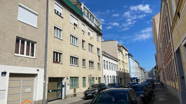 Gebäudeansicht einer Wohnstraße mit geparkten Autos und blauem Himmel.