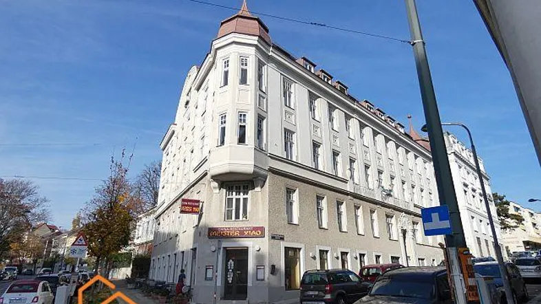 Eckgebäude mit klassischer Architektur und Geschäften im Erdgeschoss an einer belebten Straße.