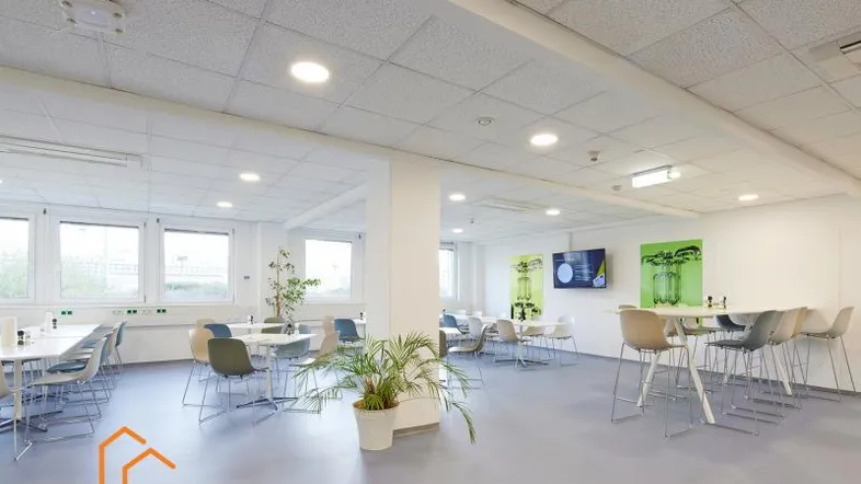 Heller, offener Bürobereich mit modernen Tischen, Stühlen und Pflanzen, ideal für Pausen oder Teamarbeit.