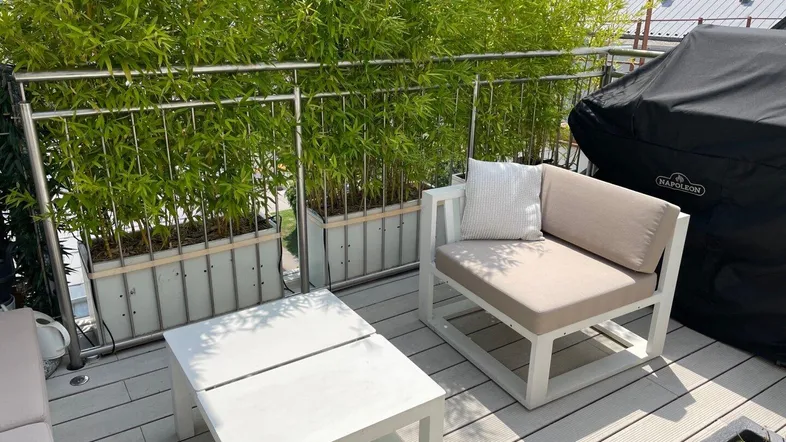 Sonnige Dachterrasse mit bequemen Gartenmöbeln und Grill, umgeben von grünen Pflanzen.