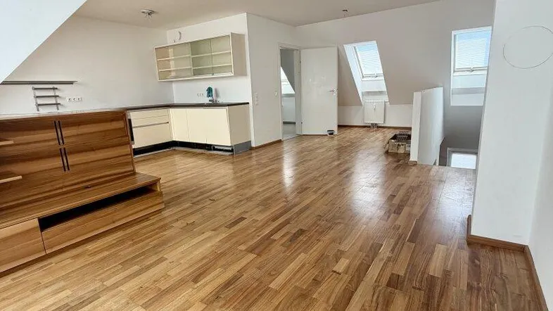 Helles Dachgeschoss-Wohnzimmer mit Holzboden und integrierter Küchenzeile unter der Dachschräge.