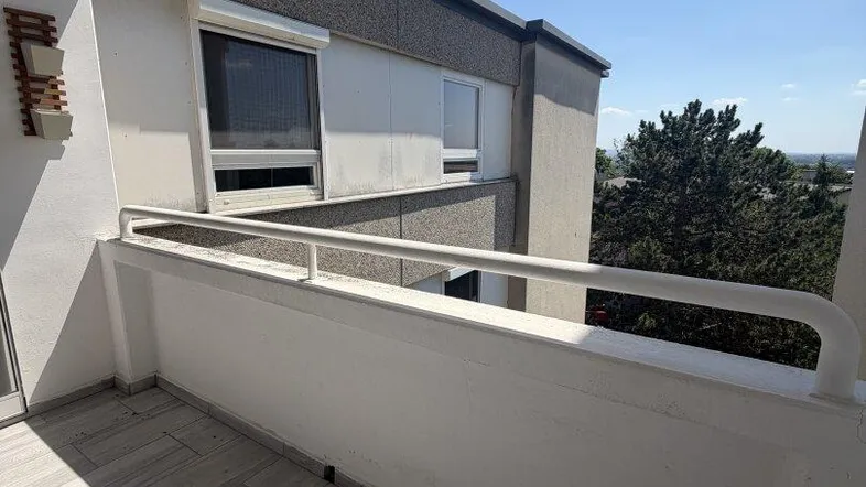 Heller Balkon mit Fliesenboden und Blick auf die Umgebung sowie weitere Gebäude unter blauem Himmel.