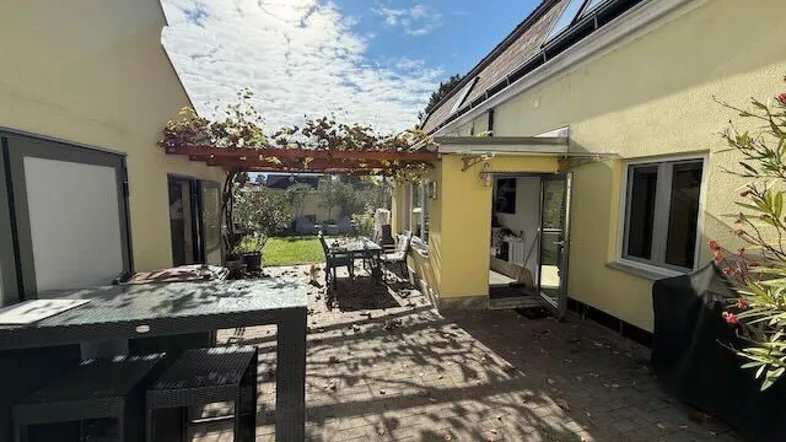 Große gepflasterte Terrasse mit Pergola und Gartenmöbeln, die zum Garten führt.