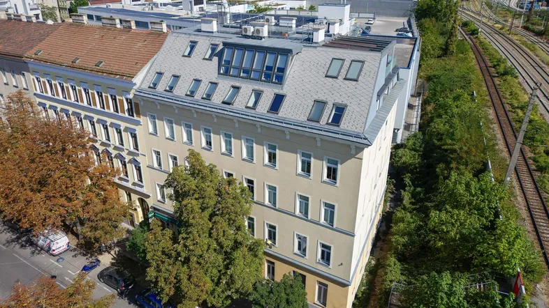 Luftaufnahme des Gebäudes mit neuem Dachausbau, umgeben von Stadtlandschaft und Bahngleisen.
