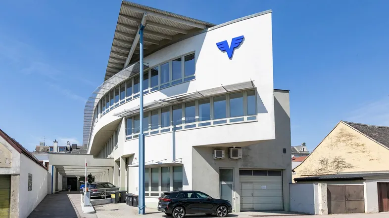 Modernes Geschäftsgebäude mit markanter Architektur, großen Fenstern und Parkplätzen davor.