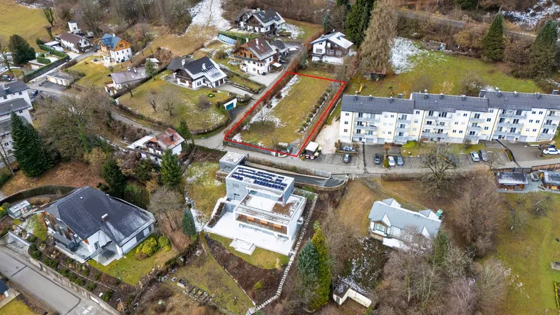 Luftaufnahme eines Grundstücks mit roter Umrandung, umgeben von Wohnhäusern und verschneiter Landschaft.
