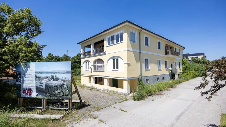 Gelbes Mehrfamilienhaus mit Balkonen und einem Bauschild im Vordergrund unter blauem Himmel.