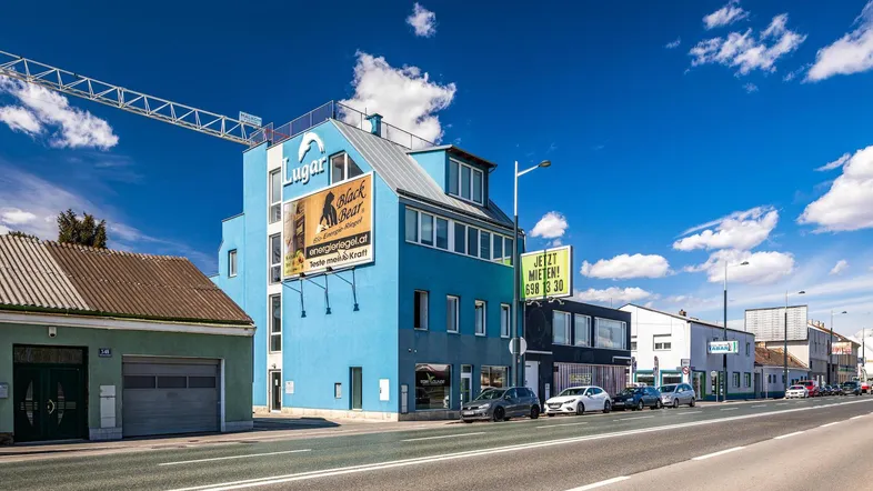 Blaues Gebäude mit moderner Architektur und Werbetafeln an einer belebten Straße unter blauem Himmel.