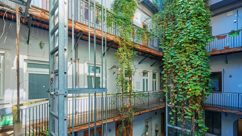 Innenhof eines Gebäudes mit üppigem Grün, mehreren Balkonebenen und einem sichtbaren Aufzug.