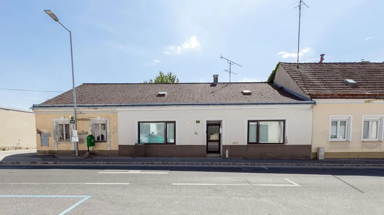Gebäudeansicht von vorne mit teilweise renovierter Fassade und direktem Zugang zur Straße.