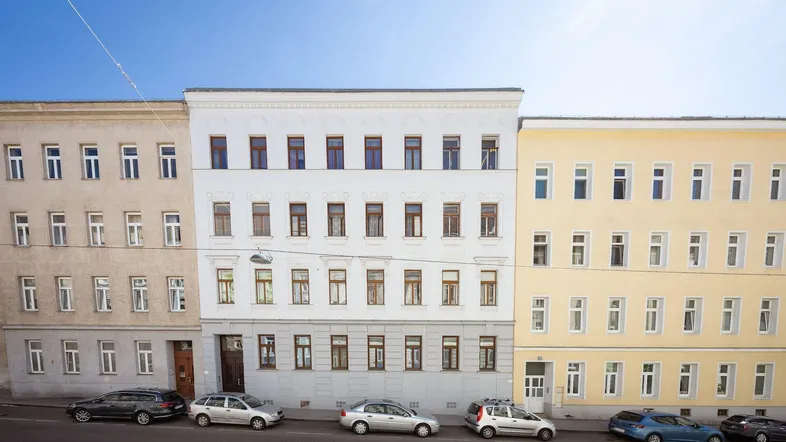 Ansicht der Gebäudefassade mit mehreren Stockwerken und parkenden Autos auf der Straße.