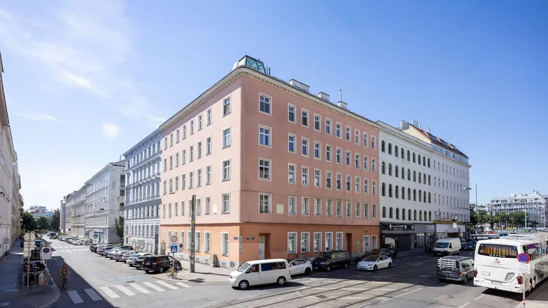 Weitläufige Straßenansicht eines Eckgebäudes in urbaner Umgebung mit geparkten Fahrzeugen.