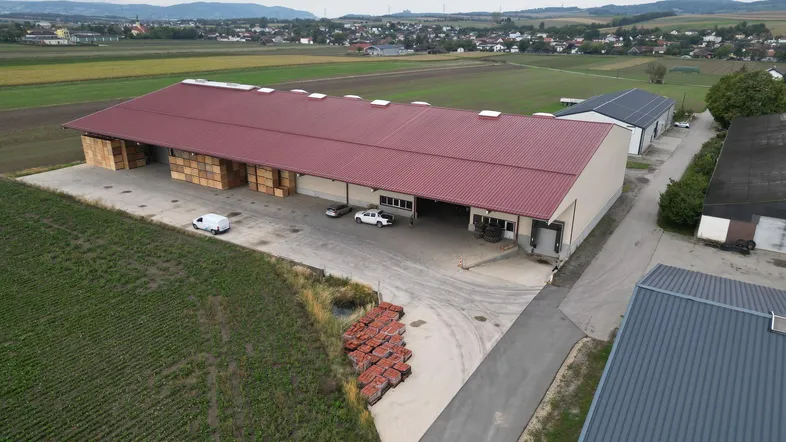 Luftaufnahme eines großen Lagergebäudes mit rotem Dach, umgeben von Feldern und ländlicher Landschaft.